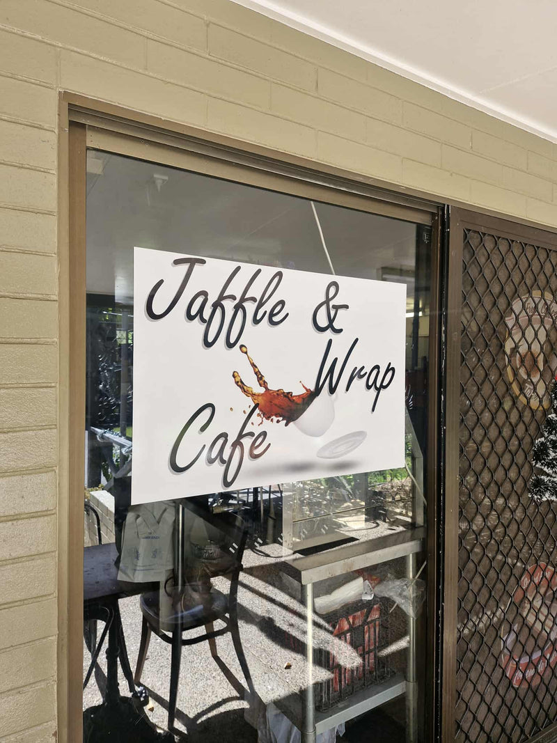 Glass door with 'Jaffle & Wrap Cafe' sign, showing interior of a cafe.
