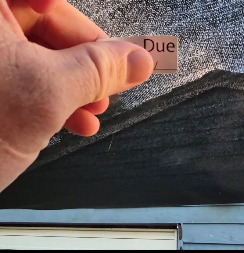 Hand holding a small rectangular card with 'rego Due' sticker against a smooth window surface.