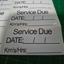 Load image into Gallery viewer, Service due label with fields for date, kilometers, and hours on a green cutting mat.
