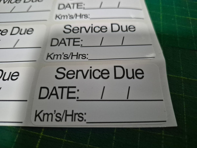 Service due label with fields for date, kilometers, and hours on a green cutting mat.