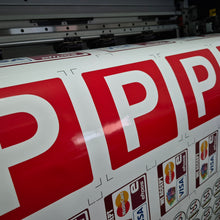 Load image into Gallery viewer, Large roll of paper with red 'P' letters and logos on a printing machine.
