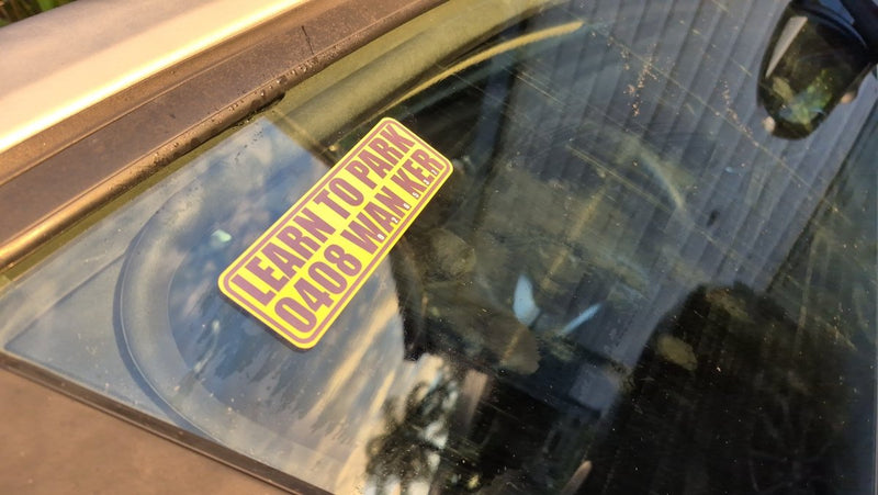 Yellow Learn to park wanker sticker sticker on a car windshield with reflections.