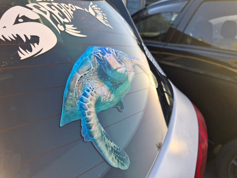Car window with a large blue and green Turtle decal on a white car.