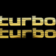 Load image into Gallery viewer, Two gold Turbo stickers flat lay black background
